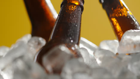 Cerca-De-Botellas-De-Vidrio-De-Cerveza-Fría-O-Refrescos-Enfriándose-En-Un-Cubo-Lleno-De-Hielo-Contra-Fondo-Amarillo